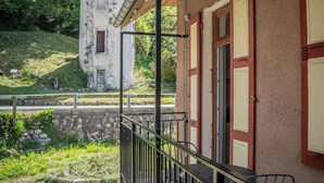 A building with a balcony, a stone wall, and a tower in the background. - Studio 2 pers en Chartreuse - balcony, village center & nature | La Borne 31 (Saint-Pierre-d'Entremont)