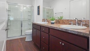 Un bagno con box doccia in vetro, lavabo con piano in marmo e specchio sopra il lavabo.