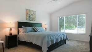 Camera da letto con un letto, due comodini, una ventola a soffitto, una finestra e un quadro appeso al muro.