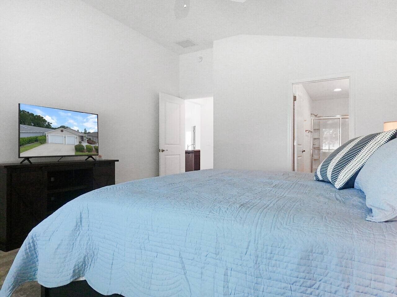 A bedroom with a bed, a television on a stand, and a door leading to another room.