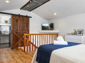 A bedroom with a bed, a TV mounted on the wall, a wooden door, and a small desk with a chair.