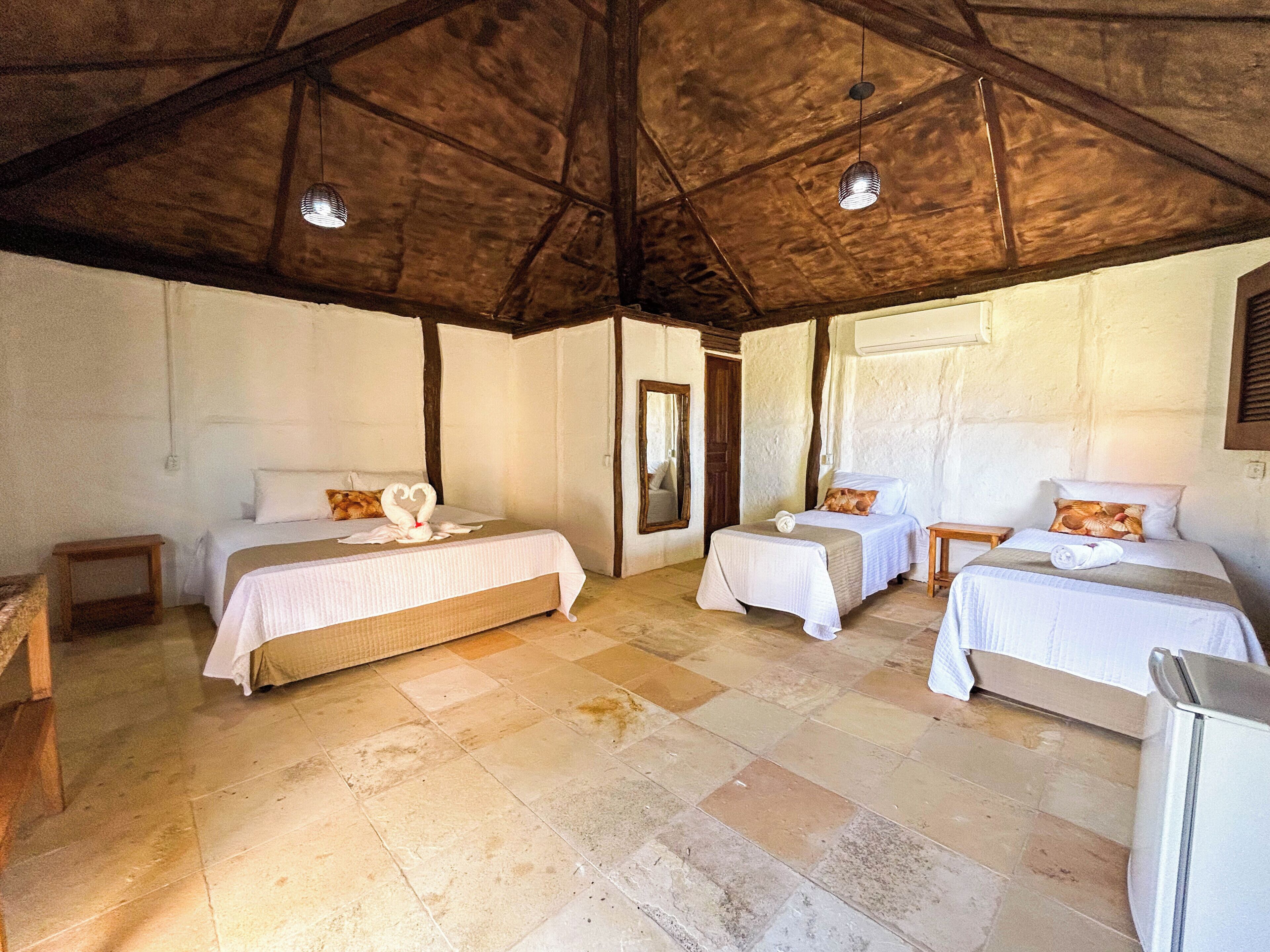 A room with two beds, a wooden ceiling, and a tiled floor.