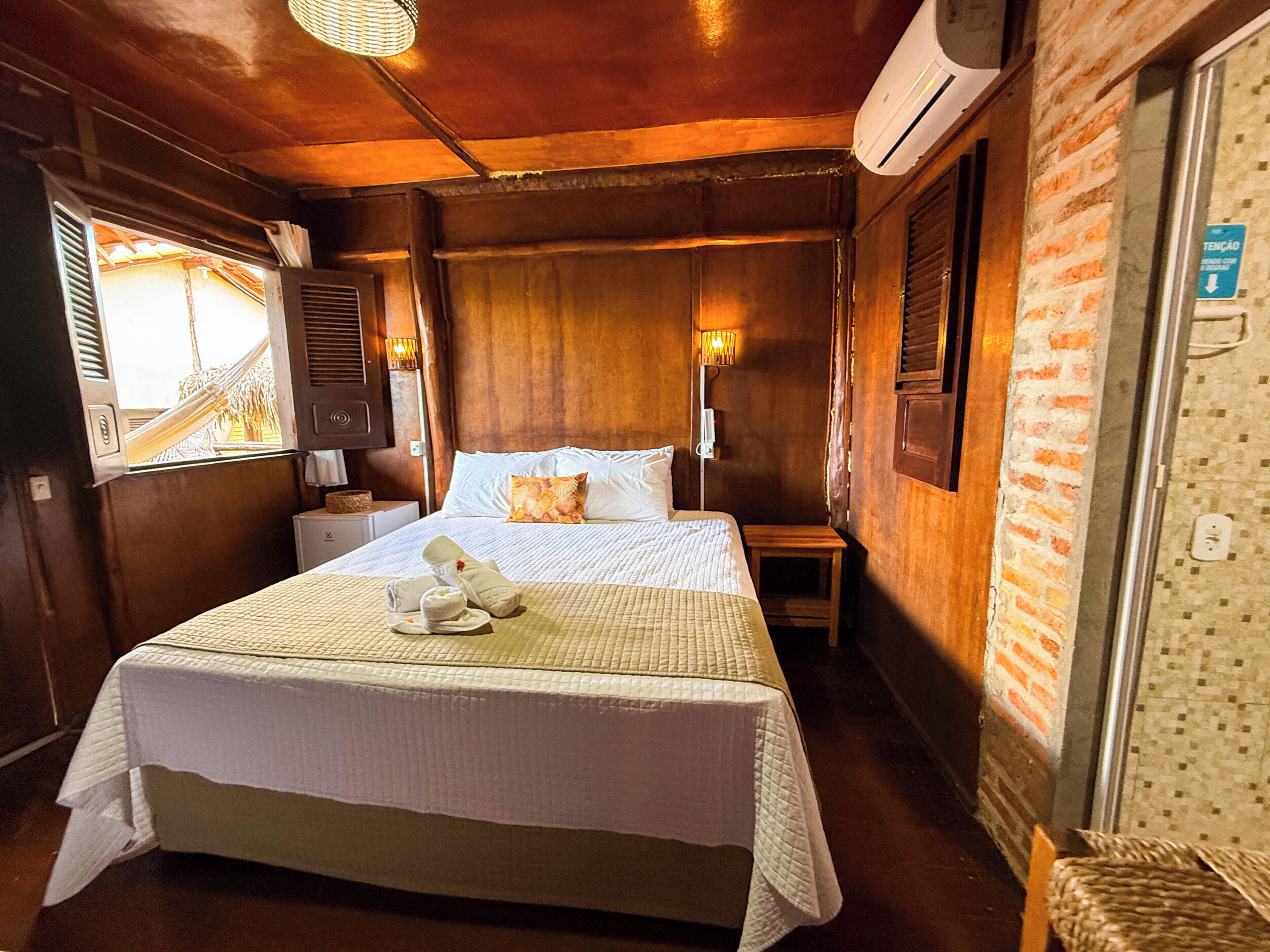 Een hotelkamer met een groot bed, een nachtkastje, een raam met luiken en een airconditioning.