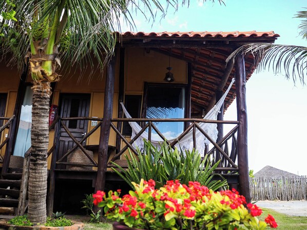 A building with a wooden balcony, a palm tree, and red flowers in the foreground.