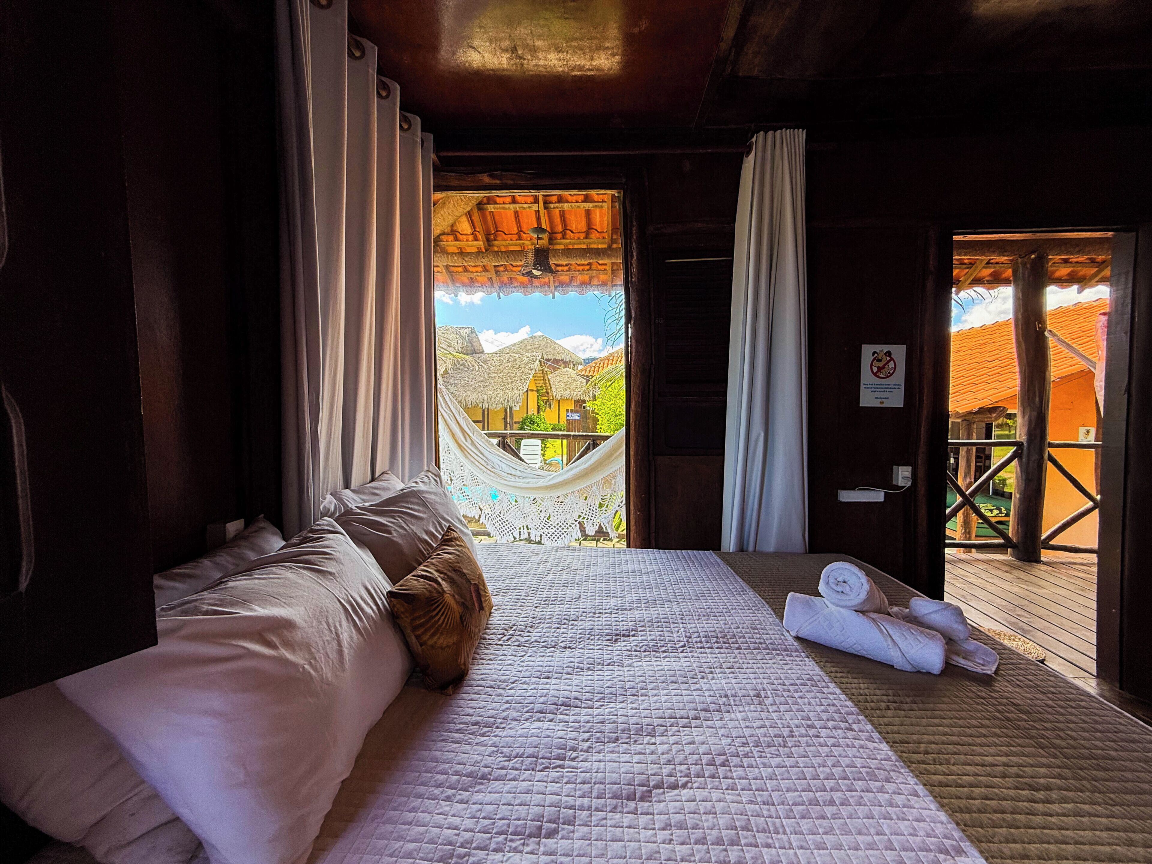 Ein Schlafzimmer mit einem Bett, einer Hängematte und Blick auf ein Gebäude mit einem Strohdach.
