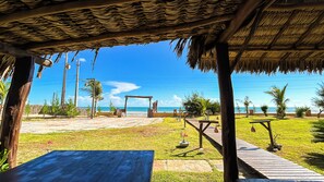 Un patio frente a la playa con techo de paja, terraza de madera y vista al océano.