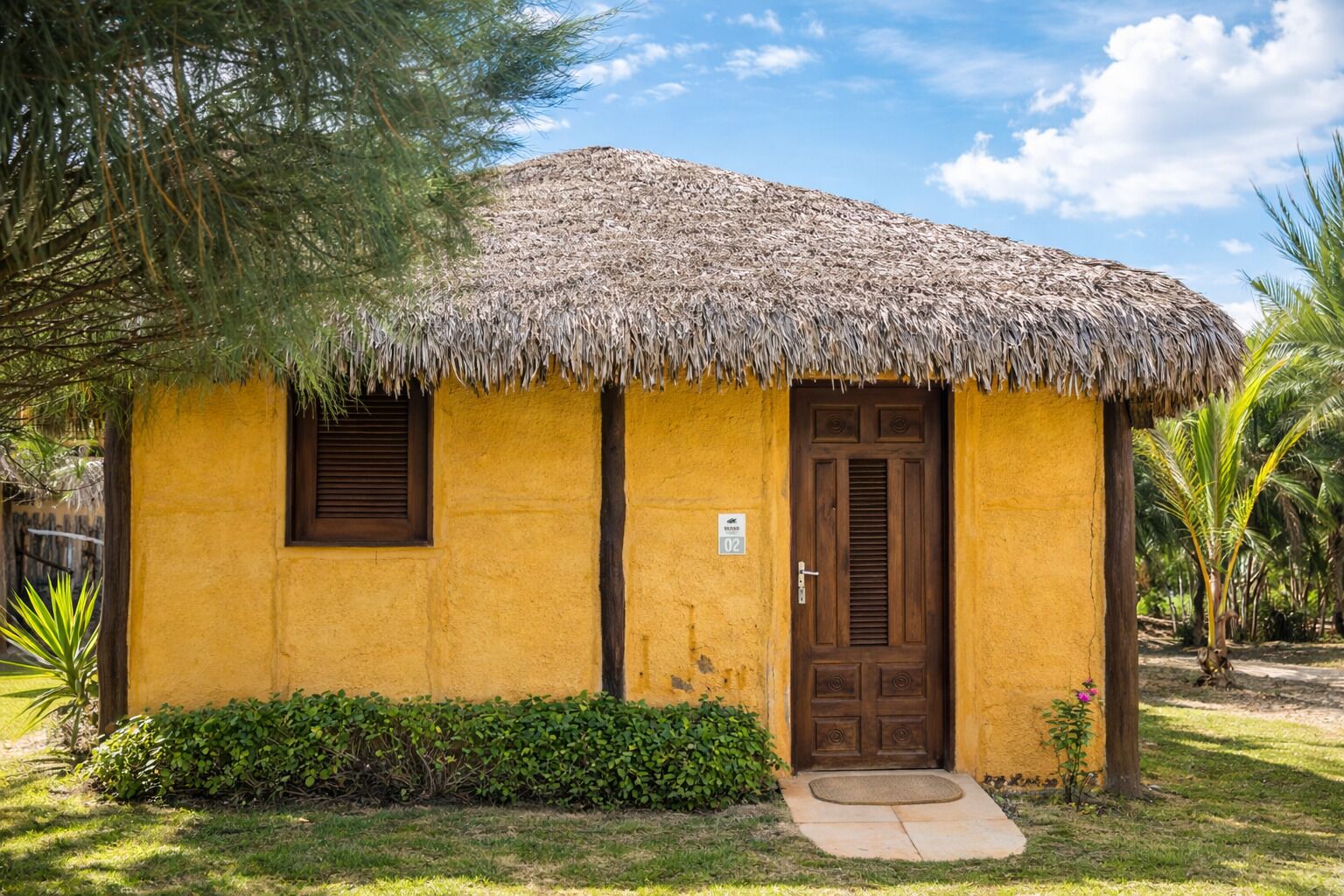 A yellow building with a thatched roof, a wooden door, and a small window.