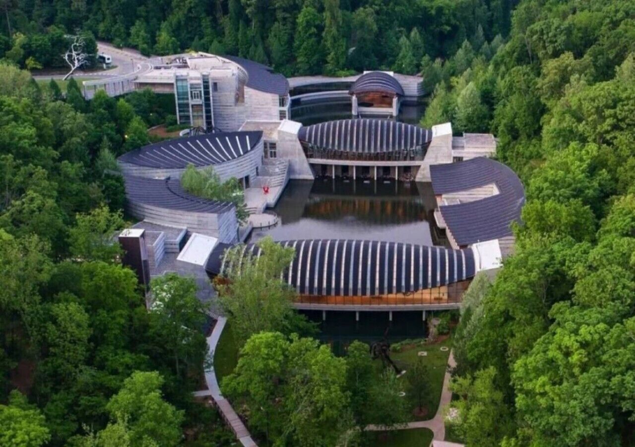 A modern building with a circular central structure surrounded by smaller buildings, set in a wooded area.