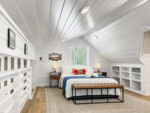 A bedroom with a sloped ceiling, a bed with a headboard, bedside tables, a bench, and a window.