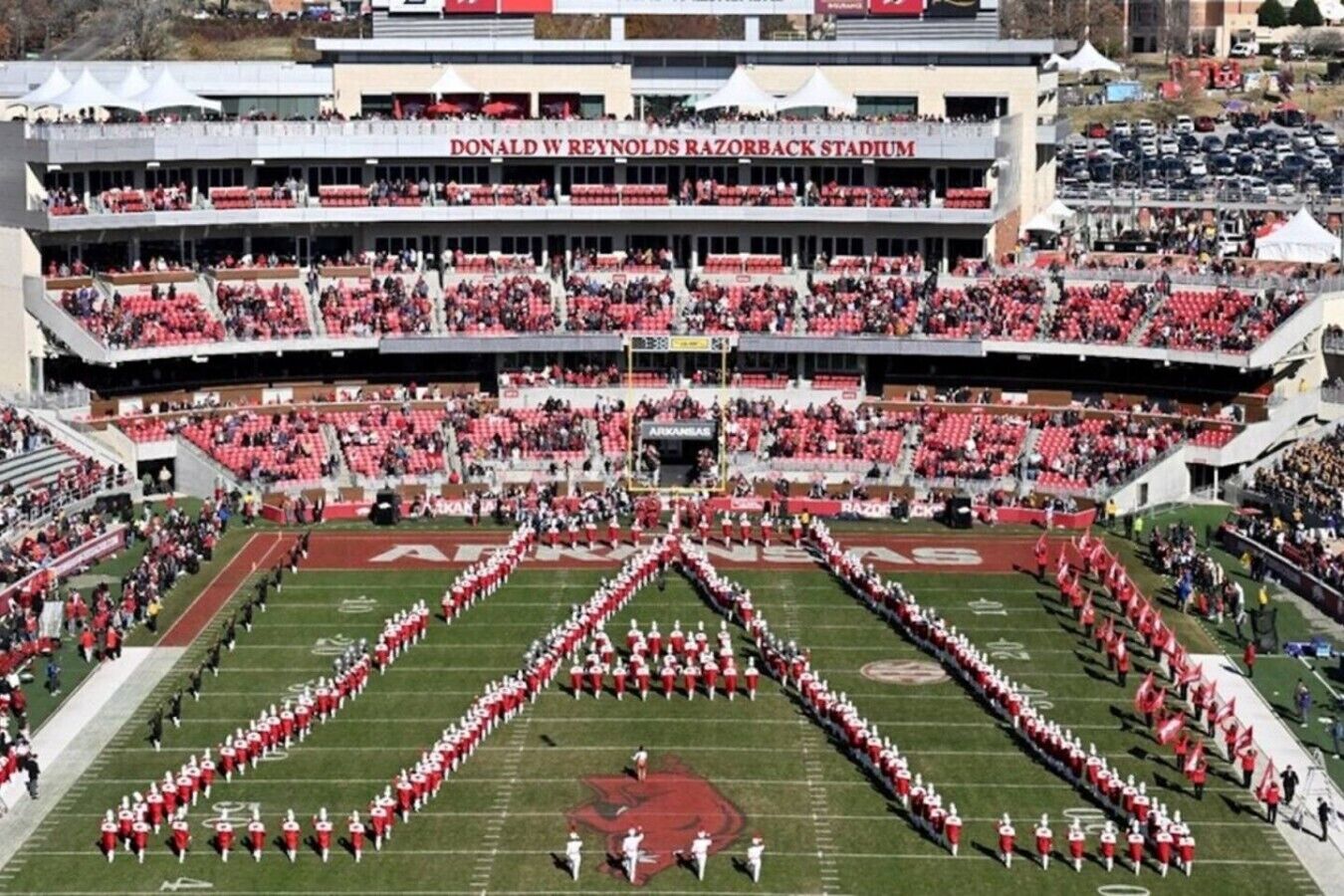 A football stadium with multiple tiers of seating, a marching band formation, and the stadium name 'DONALD W REYNOLDS RAZORBACK STADIUM' visible.