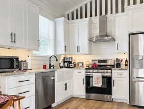 A modern kitchen with white cabinets, stainless steel appliances, and a wooden floor.