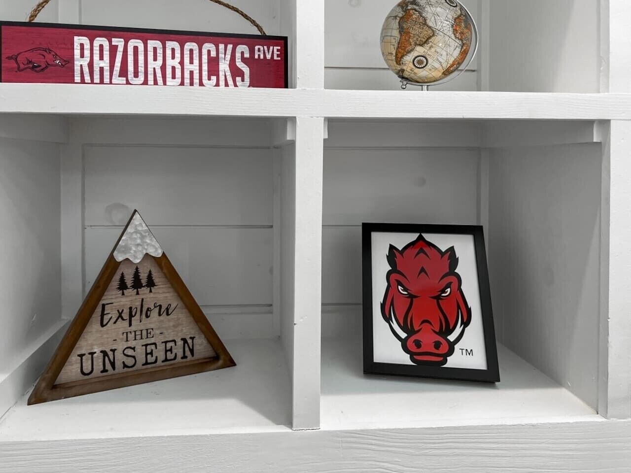 A shelf with a framed Razorbacks logo, a wooden sign with 'Explore the Unseen,' and a globe.