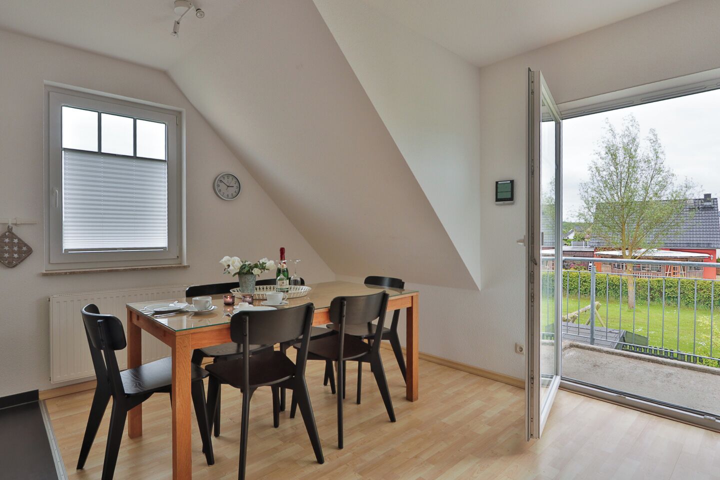 A dining area with a table, chairs, a clock, and a view of the outside.