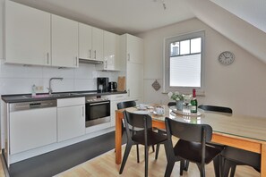 A modern kitchen with white cabinets, a built-in oven, and a dining area with a glass table and chairs. - Nice quiet apartment over 2 floors with 2 bedrooms, ideal for the family (Ostseebad Nienhagen)