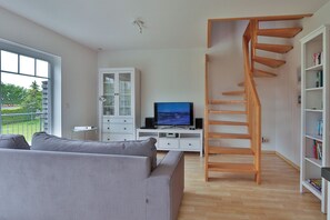 A modern living room with a grey sofa, a TV, a wooden staircase, and a white cabinet. - Nice quiet apartment over 2 floors with 2 bedrooms, ideal for the family (Ostseebad Nienhagen)