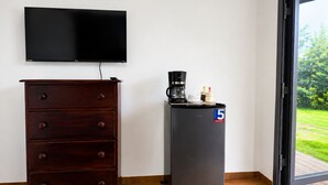 Una stanza con un comò in legno scuro, una TV a schermo piatto, una macchina per il caffè nera e un frigorifero con un adesivo '5 Grandes'.