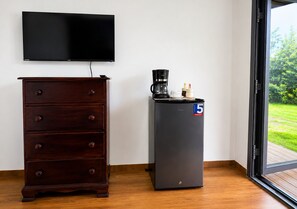 A room with a dark wooden dresser, a flat-screen TV, a black coffee maker, and a refrigerator with a '5 Grandes' sticker. - ArcaVida # 1 Jungle Container • Near Beach (Limon)