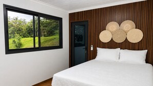 Una camera da letto con un letto, una finestra vista su vegetazione, una porta e una parete decorata con elementi circolari.