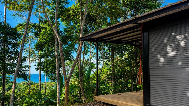 Un patio in legno coperto con vista sull'oceano, circondato da alberi e vegetazione.