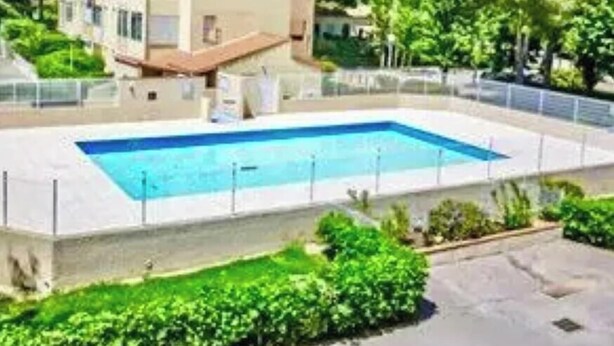 Ein zweistöckiges Gebäude mit Swimmingpool, umgeben von viel Grün.