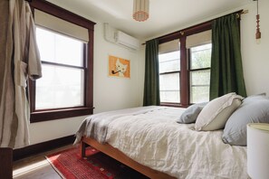 Une chambre à coucher comprenant un lit, une fenêtre, un radiateur et une œuvre d’art accrochée au mur.