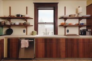 A kitchen with wooden cabinets, a stainless steel dishwasher, and shelves with dishes and cups. - The Apartment at Lucky Duck - 2 bedrooms in a historic restored bank (Carlton)