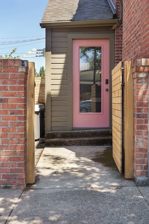 A small building with a pink door, a brick wall, and a concrete pathway leading to the entrance. - The Apartment at Lucky Duck - 2 bedrooms in a historic restored bank (Carlton)