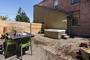 Eine Terrasse mit Tisch und Stühlen, einem Whirlpool und einem Ziegelgebäude im Hintergrund.