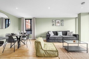 Ein modernes Wohnzimmer mit Essbereich, grauem Sofa und einem grünen Pouf.