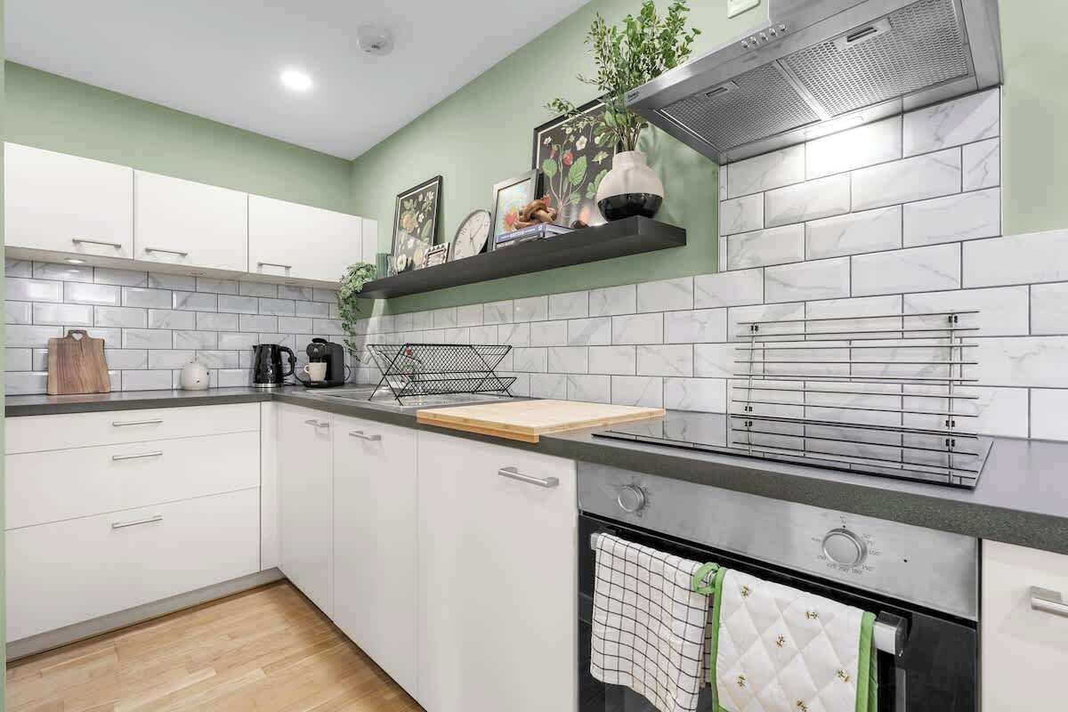 A modern kitchen with white cabinets, a black countertop, a built-in oven, and a stainless steel range hood.