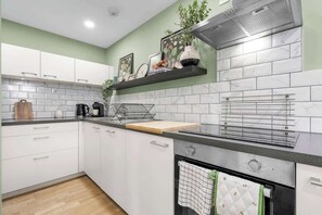 A modern kitchen with white cabinets, a black countertop, a built-in oven, and a stainless steel range hood.