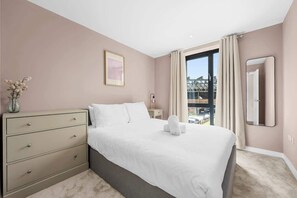 A hotel room with a bed, a dresser, a nightstand, a vase with flowers, a framed picture, a window with curtains, and a mirror.