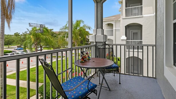 En balkon med et bord og stole, udsigt til en parkeringsplads, og en bygning med balkoner.