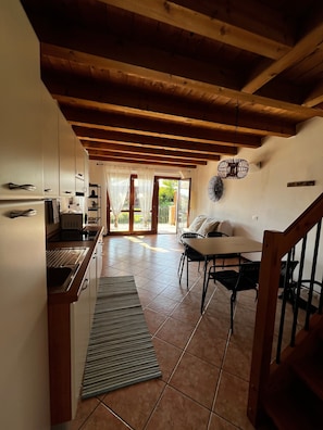 Una cucina con travi in legno, un'area pranzo con tavolo e sedie, e una vista attraverso porte in vetro.