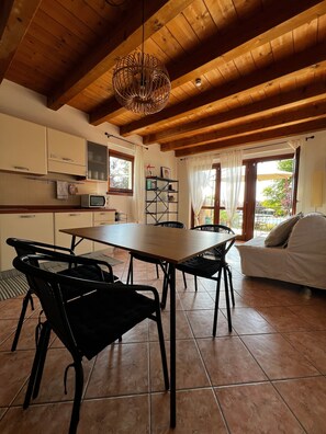 Un'ampia cucina con travi in legno, un'area pranzo con sedie, un divano e vista sull'esterno.