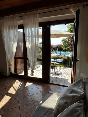 Una stanza con vista su una piscina esterna, un patio con sedie e tavoli e una porta scorrevole con tende.