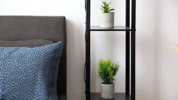 A grey sofa with a blue patterned pillow and a black metal shelf with two potted plants.