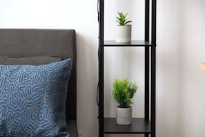 Ein graues Sofa mit einem blau gemusterten Kissen und einem schwarzen Metallregal mit zwei Blumentöpfen.