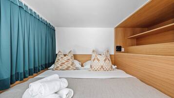 A hotel room with a bed, pillows, a wooden shelf, and a window with curtains.