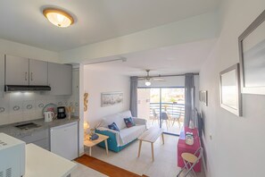 Un espacio habitable compacto con kitchenette, un sofá, una mesa de comedor y un balcón con mobiliario exterior.