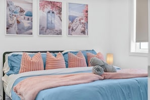 Une chambre à coucher avec un lit, des oreillers, une couverture et trois tableaux encadrés accrochés au mur.