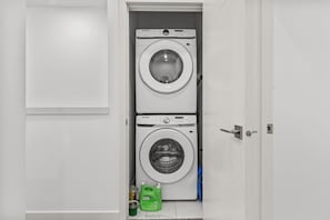 A laundry room with two stacked washing machines and a green detergent bottle. - Central 3BR Townhome | Near WEM | Family Friendly (Edmonton)
