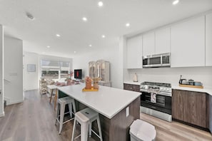 Une cuisine moderne dotée d’un îlot central, d’appareils électroménagers en acier inoxydable et offrant une vue sur l’extérieur.