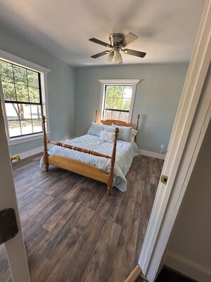Une chambre à coucher avec un lit à baldaquin en bois, un ventilateur de plafond et deux fenêtres.