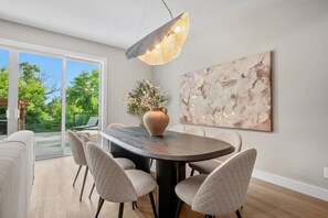 A dining area with a round table, chairs, a vase with flowers, a pendant light, and a large abstract painting on the wall. - Riverfront HotTub|7 min to Stamp|3 King Bd|Game RM (Calgary)