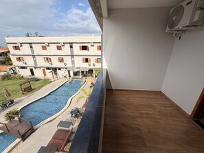A balcony with a view of a swimming pool, a building with multiple windows, and a ceiling fan. - Maresia Parque Hotel (Rio das Ostras)