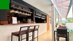 Zona de bar con mostrador, copas de vino colgantes y un espacio de asientos con sillas.
