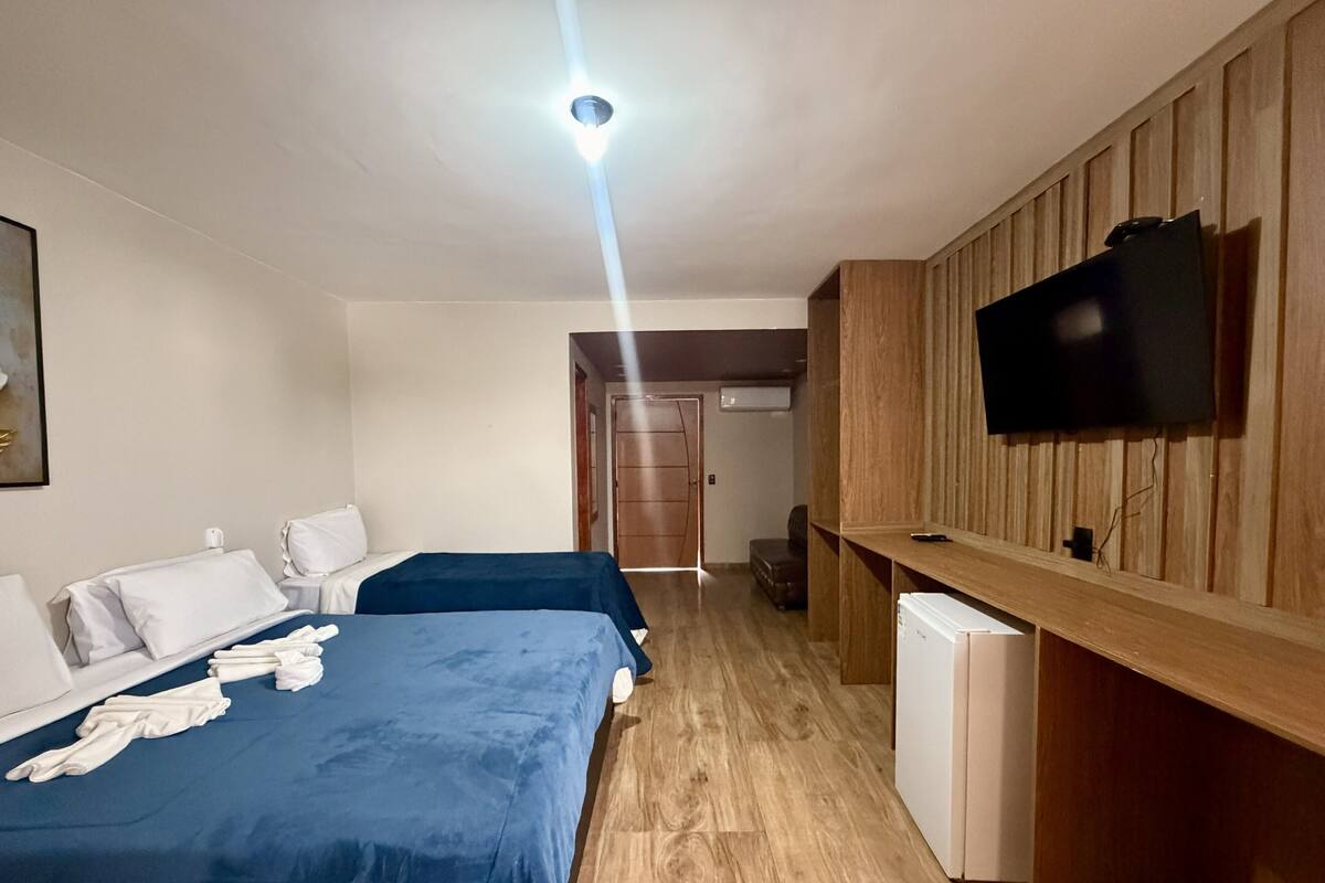 Habitación de hotel con dos camas, televisión, pared de paneles de madera y una puerta que da a otra habitación.