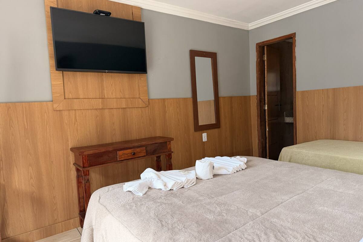Una habitación de hotel con una cama, una mesita de noche de madera, un televisor montado en la pared y una puerta.