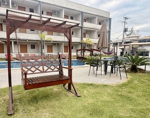 Un área de piscina con una silla hamaca, mesas, sillas y una hamaca.
